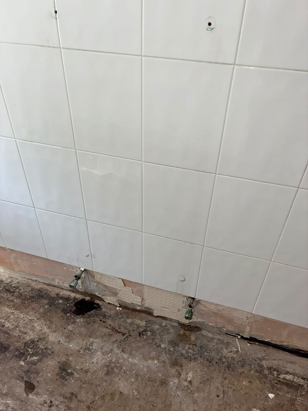 Bathroom stripped back to tiled walls and bare floor with pipe work exposed