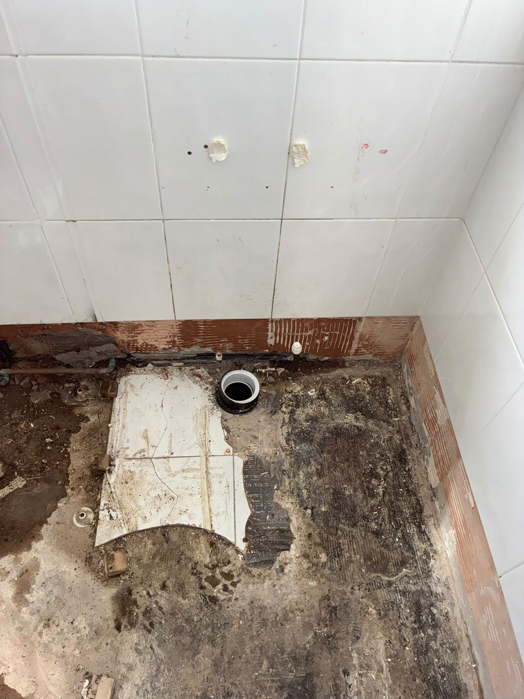 Toilet soil pipe connection exposed on a stripped bathroom floor