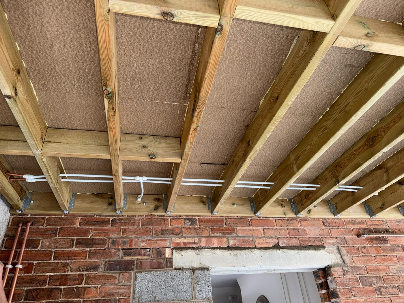 Hot and cold pipe runs threaded through new timber floor joists above a brick wall