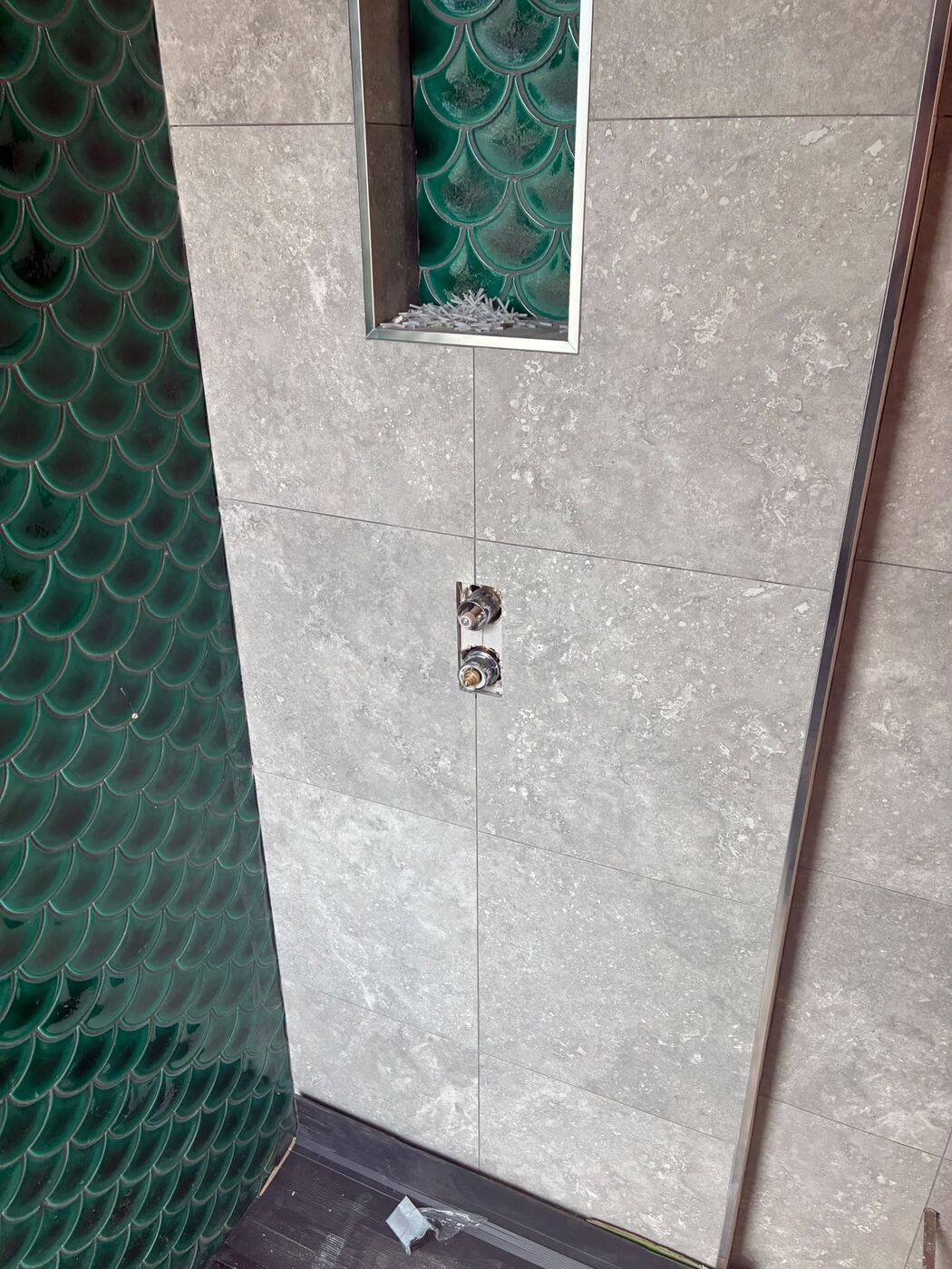 Close-up of a tiled shower niche and shower controls on grey tiles