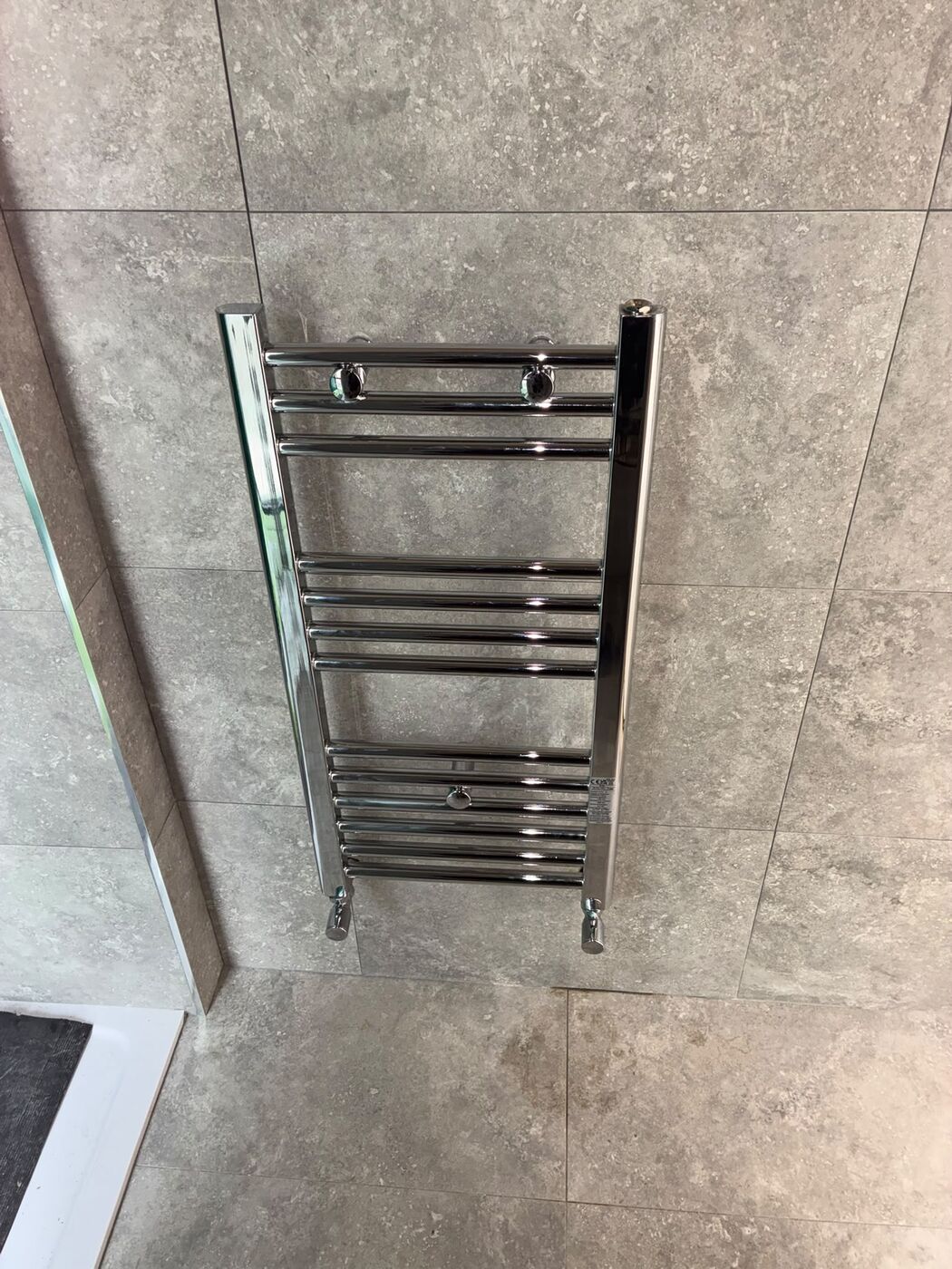 Chrome heated towel rail fitted to a grey tiled bathroom wall